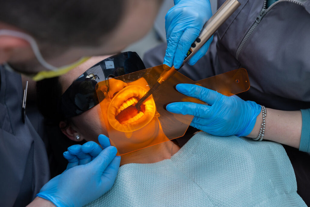 This image captures a dental procedure where professionals are attending to a patient using specialized tools and safety equipment, ensuring a thorough and safe treatment experience.