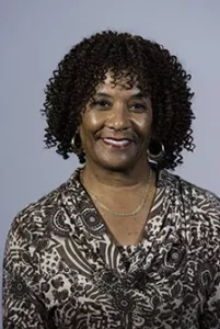 Professional headshot of a woman with curly hair wearing a patterned top