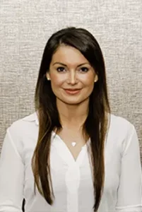 Female team member in white cardigan and necklace smiling at camera against neutral background
