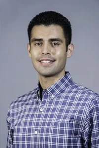Professional headshot of a man in a blue plaid shirt against a gray background