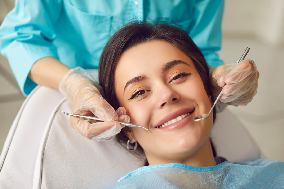 A calm young woman smiles in a dentists chair, face close-up. The dentist holds a dental mirror to the girls face. Concept teeth whitening, smile teeth, orthodontist consultation