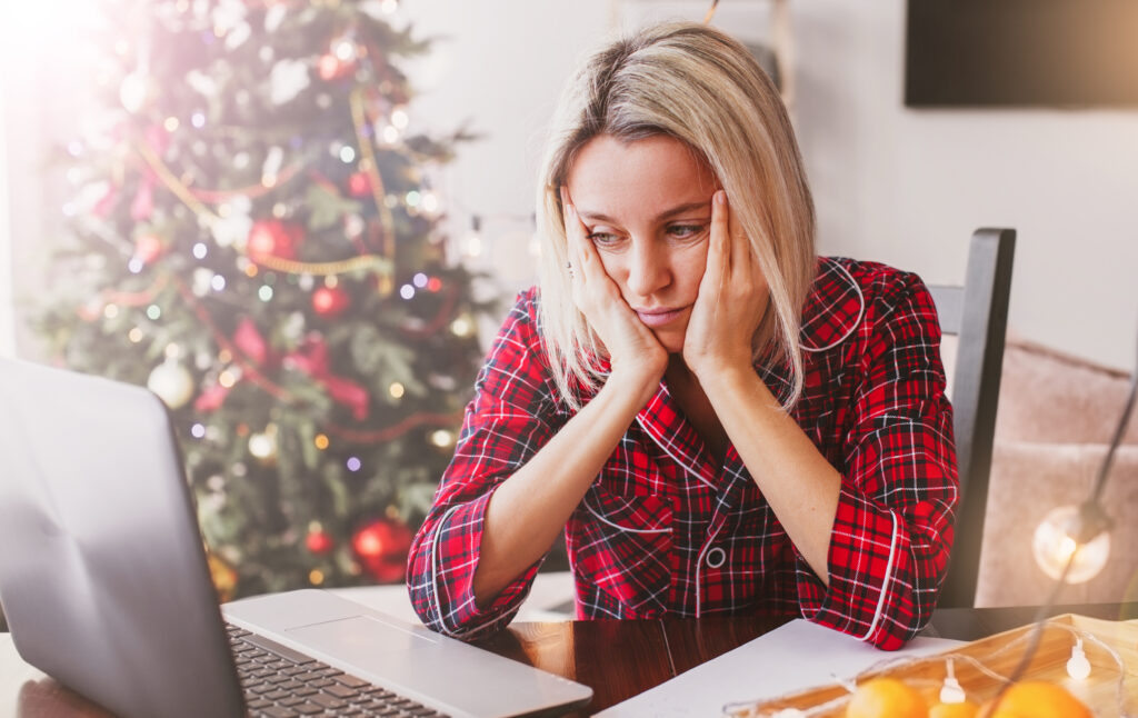Sad adult woman at home against of Christmas tree of Christmas tree. A woman is unhappy that she has to work at Christmas