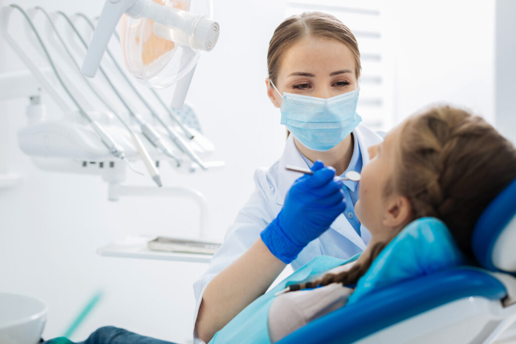Skillful doctor. Positive nice female dentist looking at her patient and treating her teeth while being at work