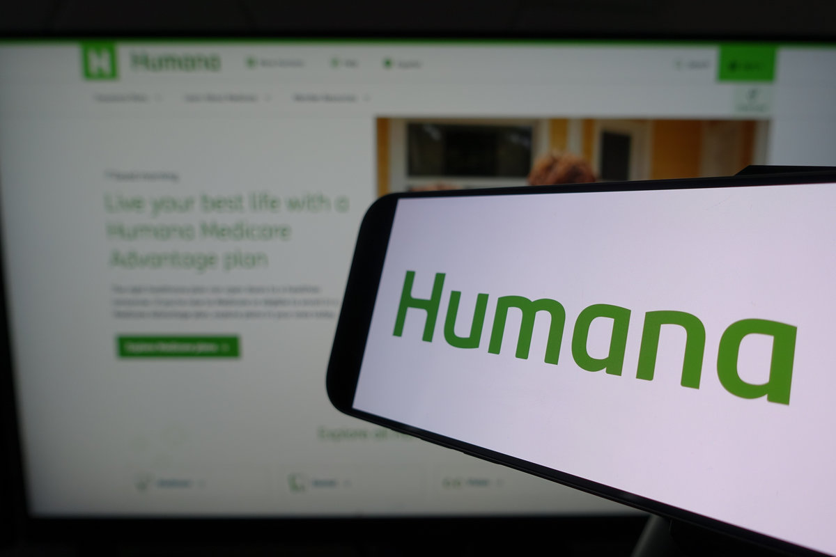 Kiel, SH, Germany March 24 2025: Smartphone displaying Humana logo in front of company website on a monitor, illustrating digital interaction and branding in a business environment.