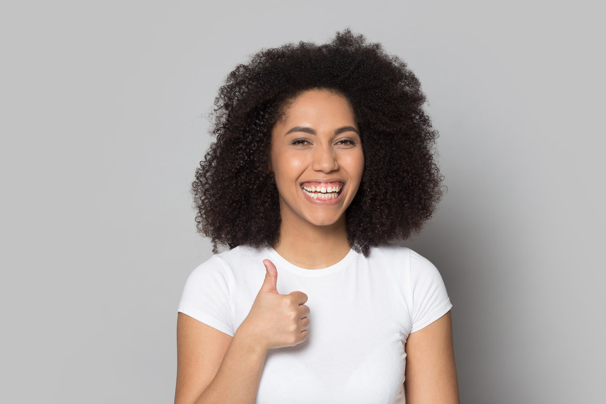 Smiling african American young woman isolated on grey studio background show thumbs up recommend good service, happy biracial millennial girl look at camera laughing give sincere recommendation