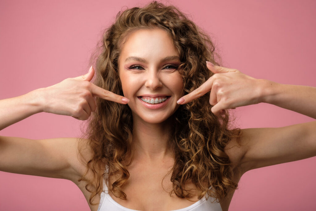 Happy curly girl with her dental braces pointing her finger to her smile