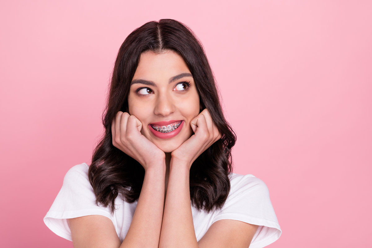 Photo of adorable happy young woman look empty space wear teeth braces isolated on pink color background.