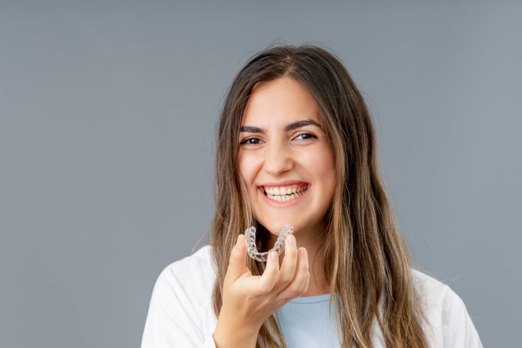 Beautiful smiling Turkish woman is holding an invisalign bracer in a grey background studio with copy space