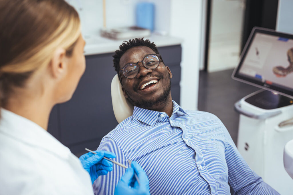 Female dentist with happy male patient at clinic. Happy patient sitting on chair while looking at dentist in medical clinic. Cheerful african american man with during examination in dental clinic